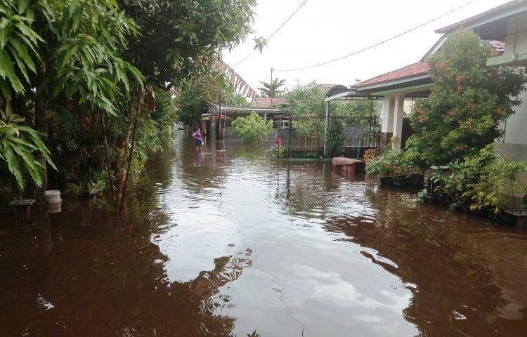 Warga tengah melintas di halaman rumah yang terendam banjir di Kota Palangka Raya, Rabu (4/12/2019)